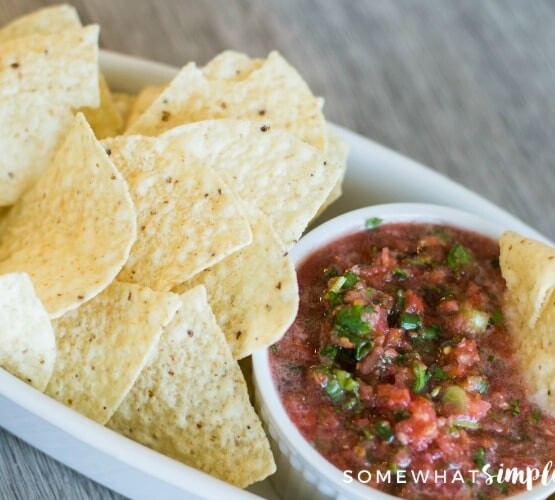 a small white bowl of fresh homemade mild salsa inside a larger white serving tray filled with tortilla chips.