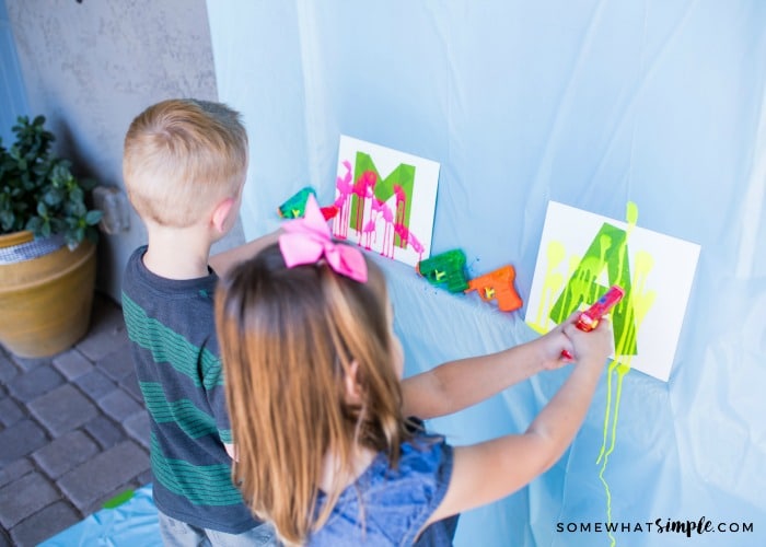 a young boy and girl shooting paint from water guns at a canvas on a wall