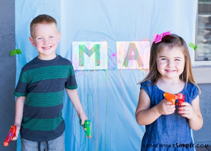 two cute children holding water guns in their hands with a water gun art project set up behind them