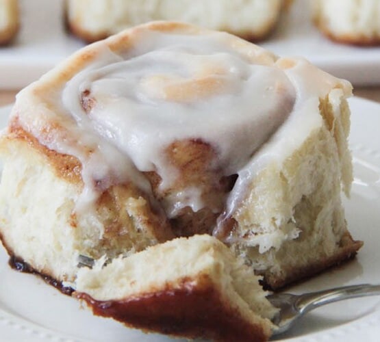 a forking cutting off the corner of a cinnamon roll with a cream cheese frosting on top