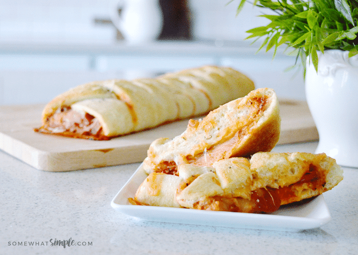 a full calzone in the background on a cutting board and slices of calzones on a plate filled with cheese and peperroni made from this easy calzones dinner recipe
