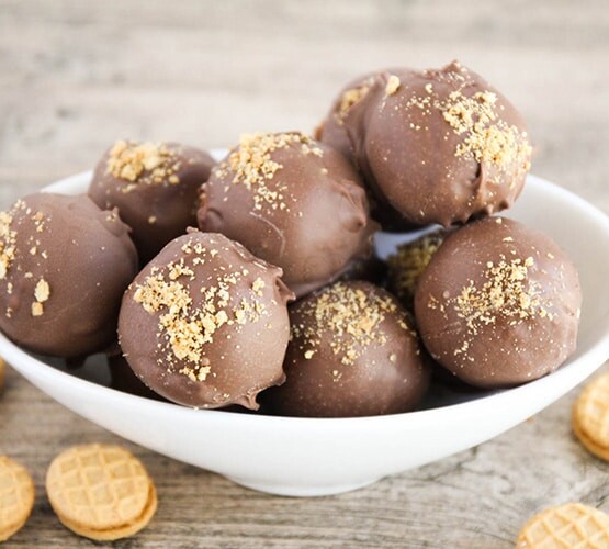 a white bowl filled with nutter butter balls covered in chocolate. Individual nutter butter cookies are scattered on the table around the bowl.