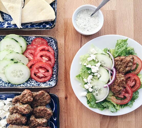 a plate filled with this easy Gyro Salad Recipe next to serving trays filled with the ingredients to make this greek salad as well as a small dish filled with tzatziki dressing