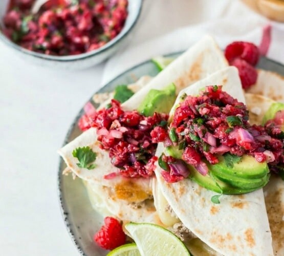 a plate piled high with slices of quesadillas topped with a raspberry salsa and slices of avocado