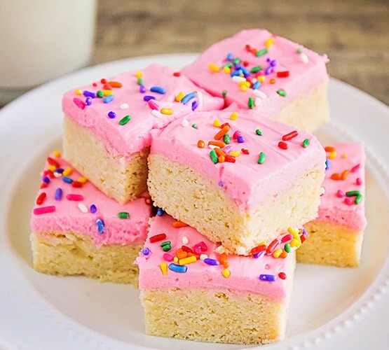 a plate of old fashioned sugar cookies topped with pink frosting and colorful sprinkles