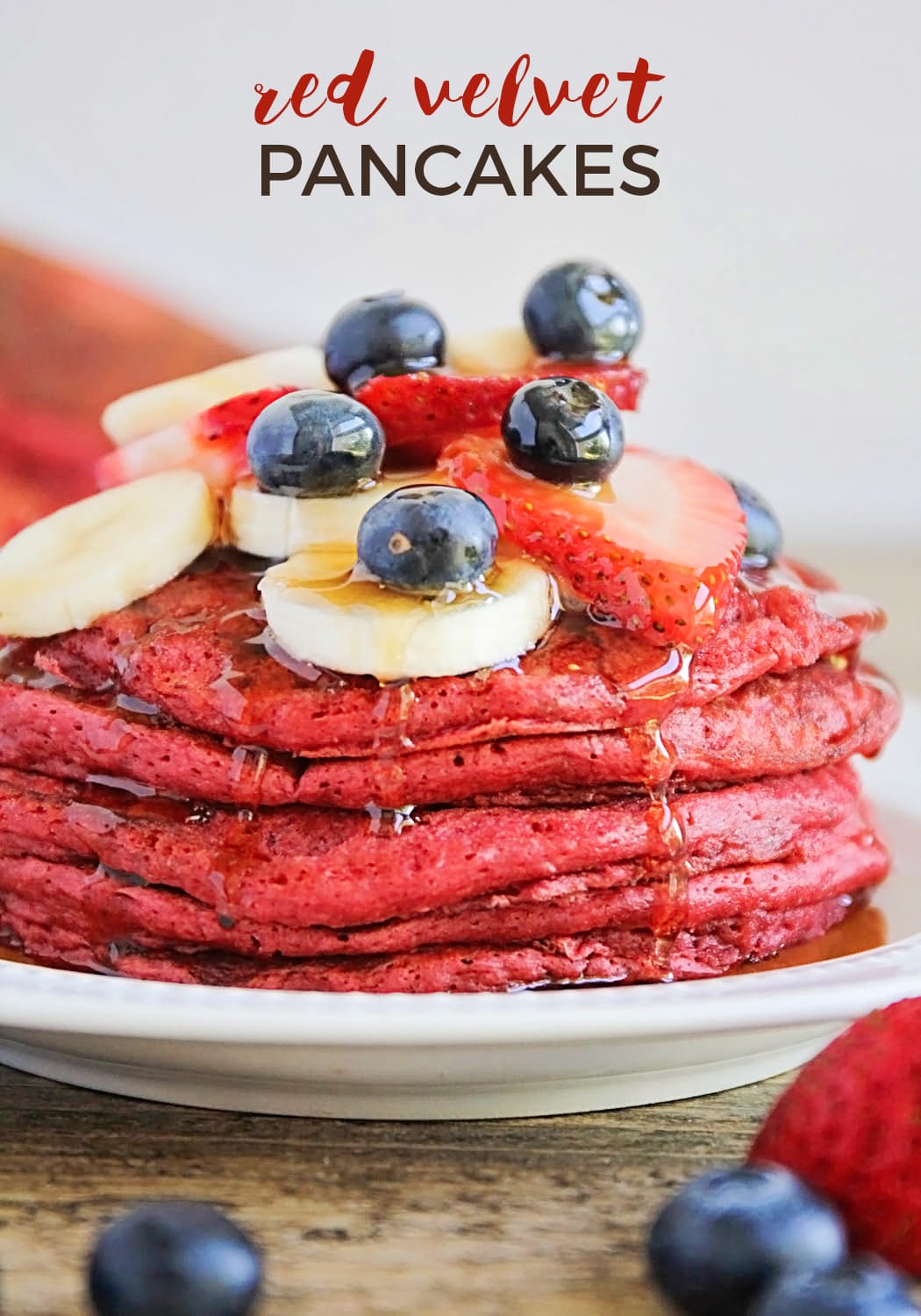 a stack of Red Velvet Pancakes on a plate topped with fresh fruit
