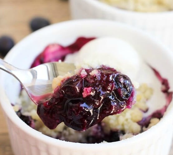 a spoon scooping out a bite of blueberry crumble out of an individual serving in a white ramekin