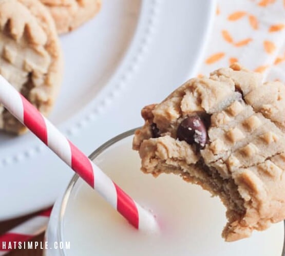 a peanut butter cookie with chocolate chip with a bite taken out of it sitting on the rim of a glass of milk