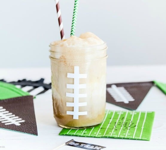 a mason jar painted to look like a football with a foaming drink inside