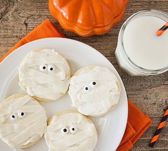 Halloween Mummy sugar Cookies on a plate next to a glass of milk