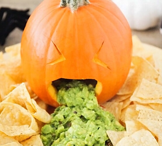 a barfing pumpkin with guacamole coming out of it's mouth with tortilla chips spread all around