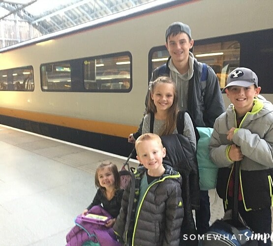 five children standing on the Eurostar train platform in London. Behind them is a high speed train that is headed to Paris.