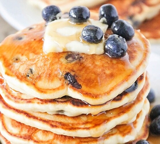 a stack of lemon blueberry pancakes topped with a pad of butter, syrup and fresh blueberries