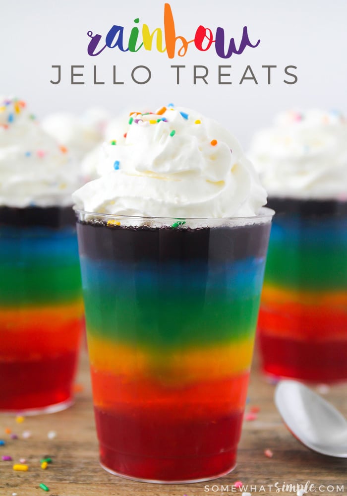 a close up of a rainbow jello dessert cup with two more in the background. All are topped with whipped cream and the words rainbow jello treats is written at the top of the image