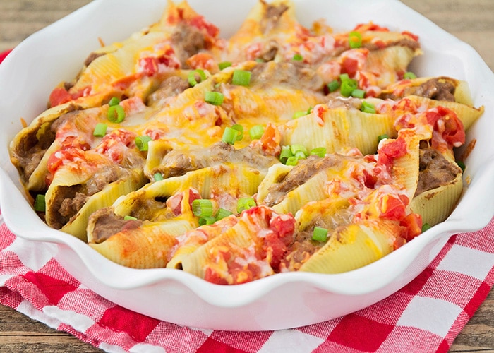 a casserole dish full of taco stuffed pasta shells covered with cheese, green onions and salsa