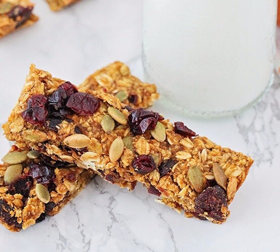 two homemade pumpkin granola bars laying on a counter top next to a glass of milk