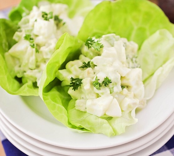 looking down on a stack of white plates with two large leaves of lettuce on top with each filled with a serving of Avocado Egg Salad