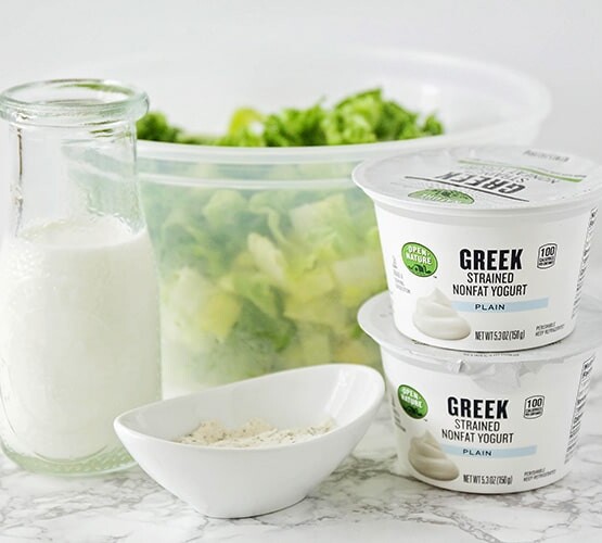 a jar of homemade ranch dressing that's next to a tub of Greek yogurt and a bowl of lettuce