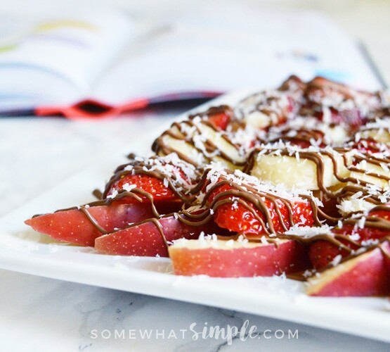 a plate of apple nachos topped with slices of strawberries and bananas, shredded coconut and chocolate drizzled over the top