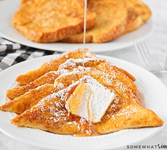 four slices of pumpkin french toast on a plate topped with a pad of butter and syrup being drizzled over the top