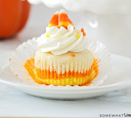 a Candy Corn Cupcake with orange, yellow and white layers on a plate topped with cream cheese frosting