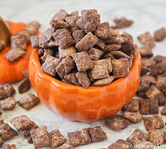 Pumpkin Spice Muddy Buddies in a pumpkin jar with some spilled on the table around it