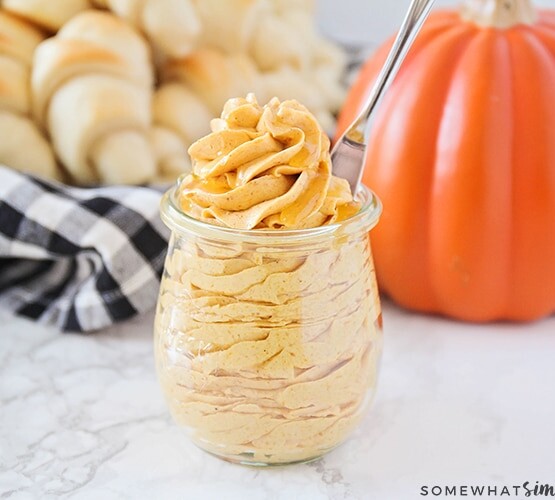 piped Whipped Pumpkin Honey Butter inside a glass jar in front of a basket of dinner rolls