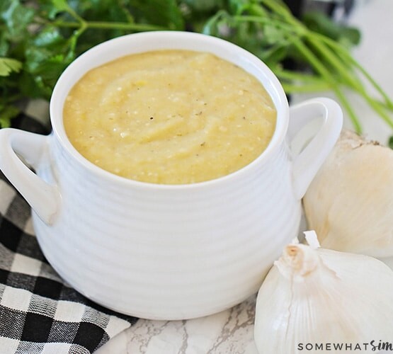 a white gravy boat filled with homemade green enchilada sauce. Next to the gravy boat are two white onions, a parsley bunch and a black and white checkered cloth napkin.