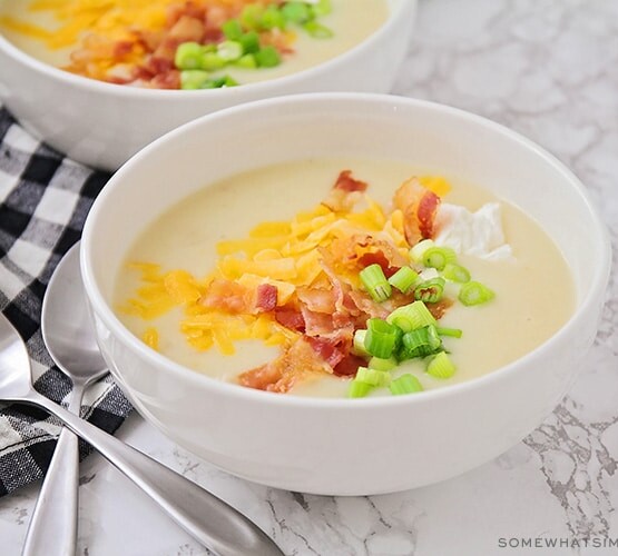 a bowl of baked potato soup topped with shredded cheese, bacon, green onion and sour cream