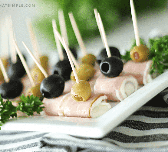 ham and cream cheese roll ups topped with black and green olives on a white serving tray