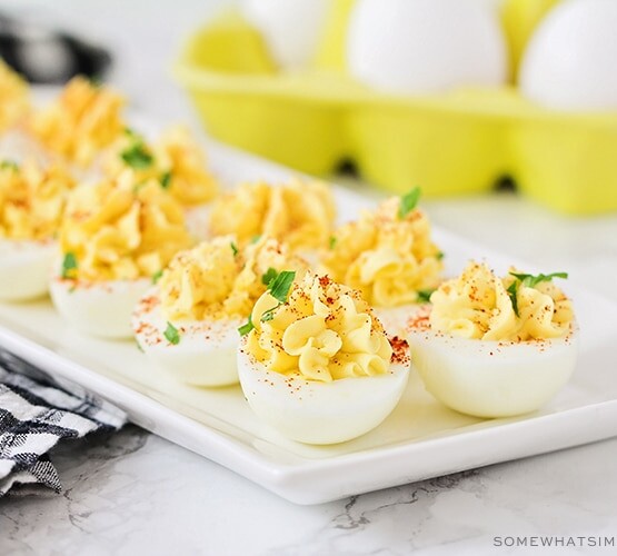 a long white serving tray filled with classic deviled eggs topped with paprika and parsley