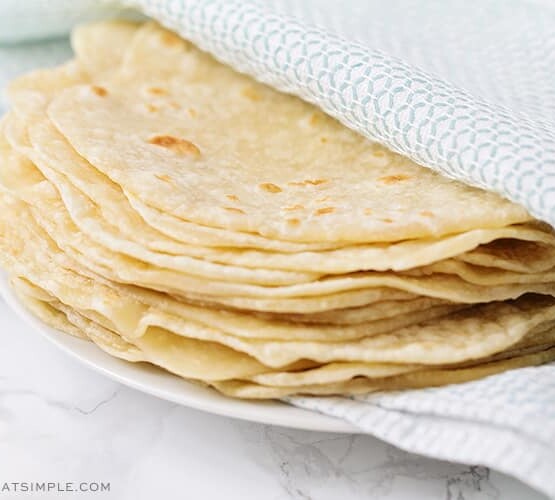 a stack of homemade flour tortillas wrapped in a blue and white towel on a white plate