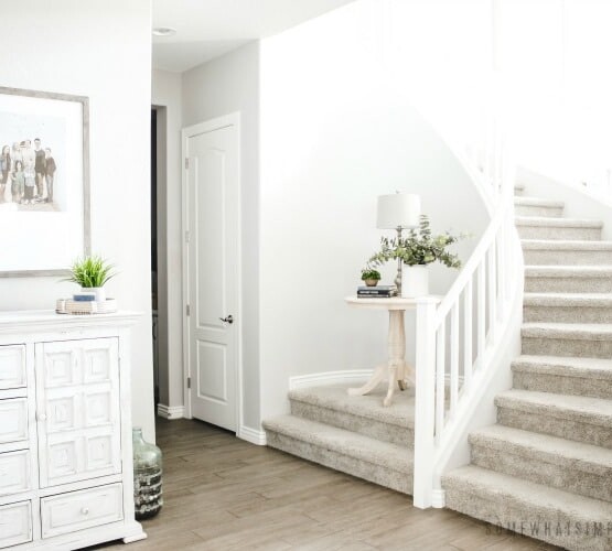 the entry way of a home with a winding staircase. A small wooden table is on an elevated landing. There is also a large white cabinet along the wall in the entry way.