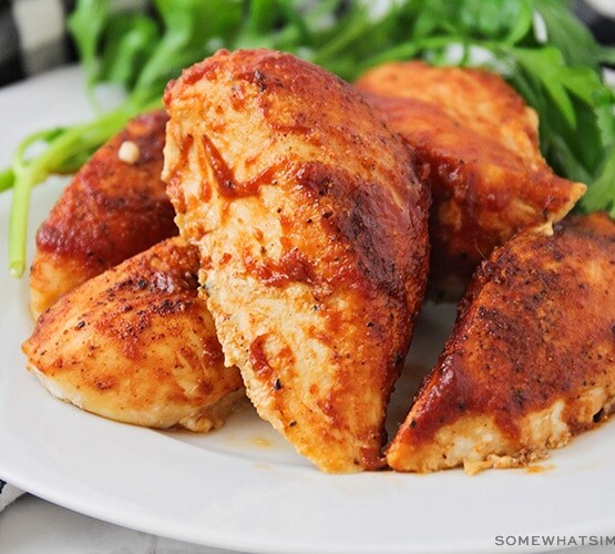 a white plate filled with baked bbq chicken breasts with leaves of green salad next to it on the plate.