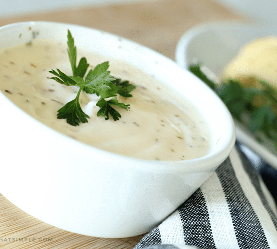 a small white bowl filled with a homemade Alfredo sauce topped with a small piece of parsley for garnishment