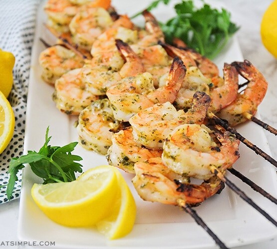 several skewers of grilled pesto shrimp fresh off the BBQ and laying on a white serving platter.