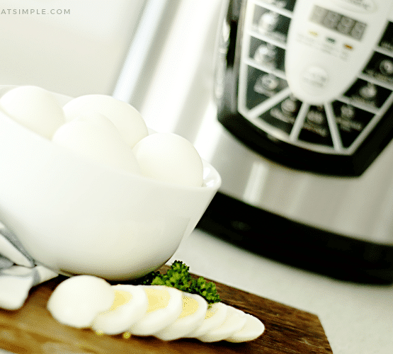 a bowl of hard boiled eggs in front of an instant pot. One of the eggs has been cut into slices and layed out on a cutting board in front of the bowl.