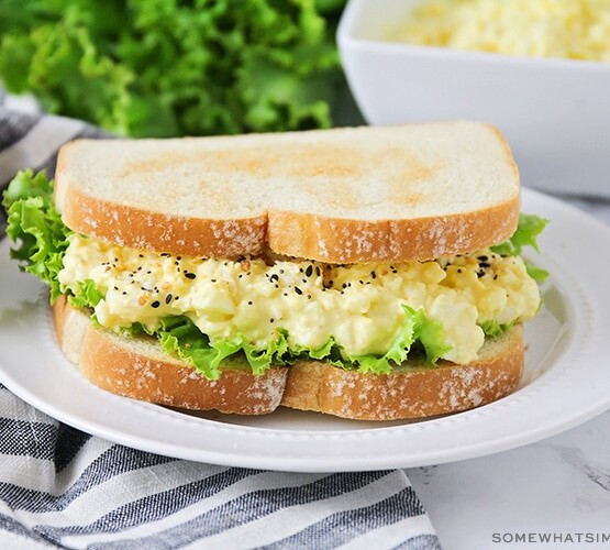 an egg salad sandwich on a white plate topped with lettuce on toasted white bread