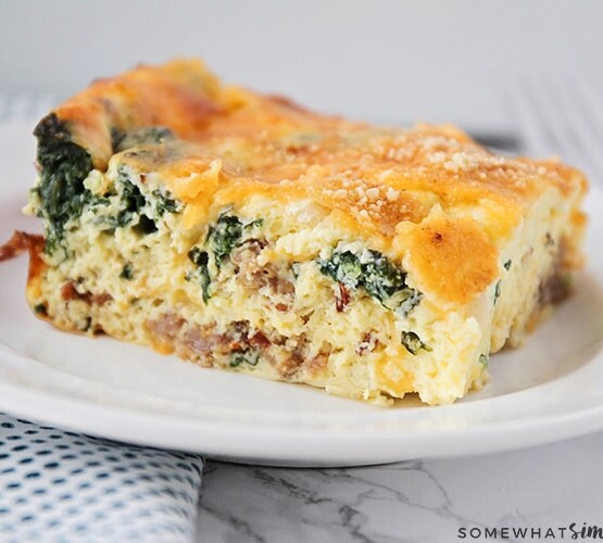 a square of spinach and egg casserole on a white plate. The casserole is topped with bread crumbs and cheese.