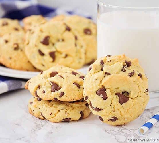 a few cake mix chocolate chip cookies on the counter next to a glass of milk with a plate full in the background.