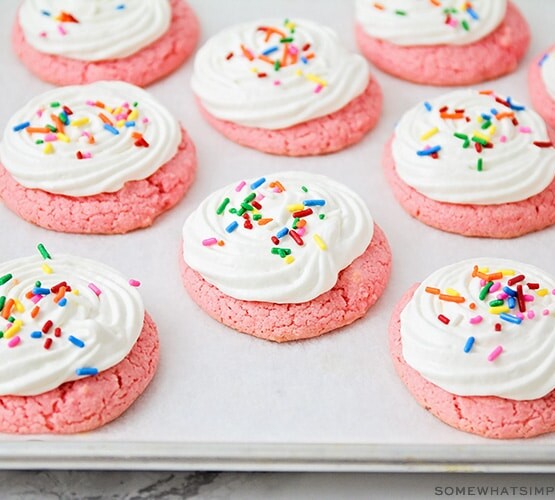 a cooking sheet filled with strawberry cake mix cookies topped with white frosting and colored sprinkles