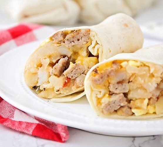 a breakfast burrito filled with potatoes, eggs, sausage and cheese that has been cut in half and is sitting on a white plate