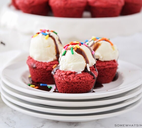 three small red velvet cake mix brownies on a stack of plates and topped with a scoop of ice cream, sprinkles and chocolate syrup