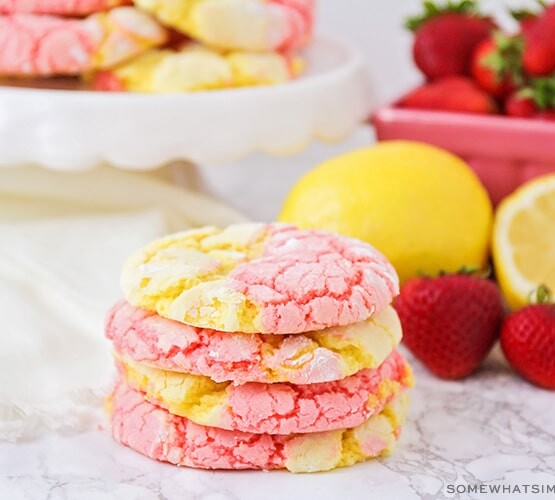a stack of strawberry lemonade cookies on a counter next to strawberries and lemons