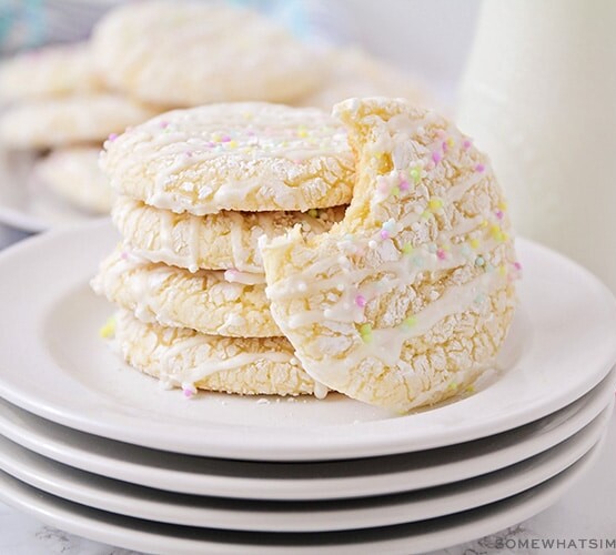 a stack on white cake mix cookies on a plate topped with a white glaze drizzled on top and pastel colored sprinkles