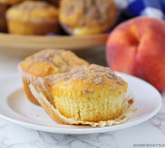 two peach muffins on a white plate with a streusel topping