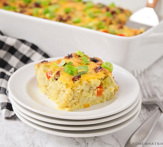 a square of tater tot breakfast casserole with pieces of bell peppers and sausage on a stack on white plates