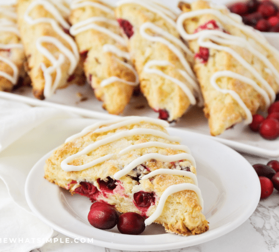 Cranberry White Chocolate Scone plated on a white plate with a serving platter of even more in the background