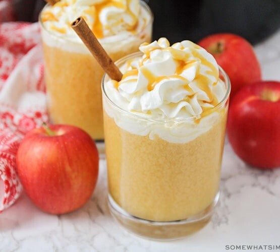 a glass of apple cider topped with whipped cream and caramel